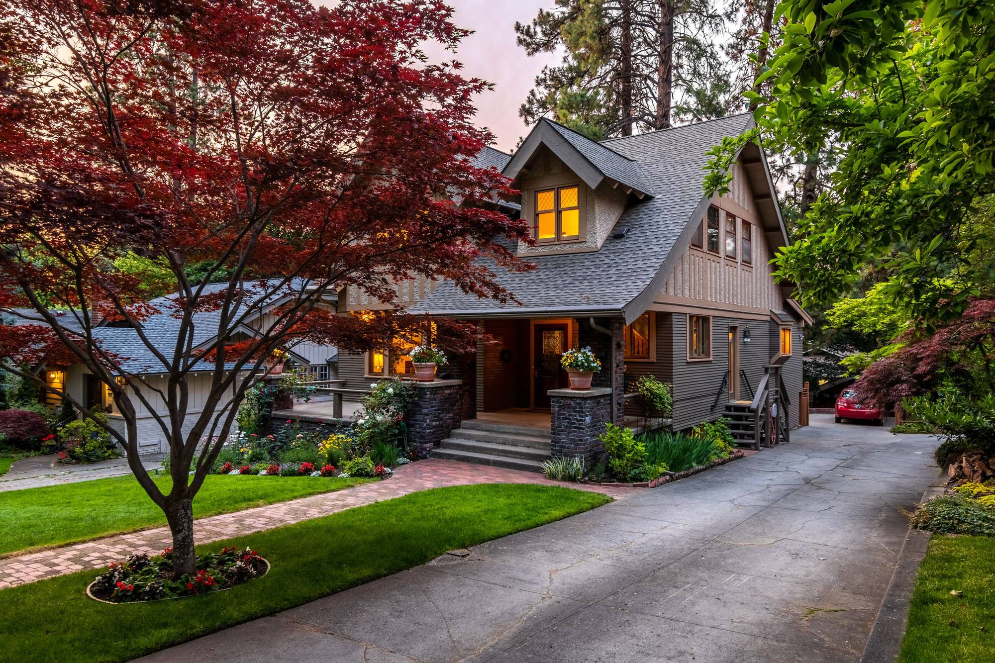Craftsman-style home at dusk with lit windows and a red Japanese maple